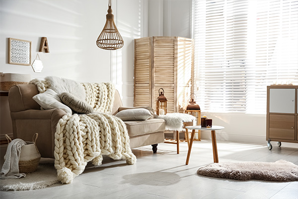 Bright living room with a beige sofa, cozy blankets, and window blinds.