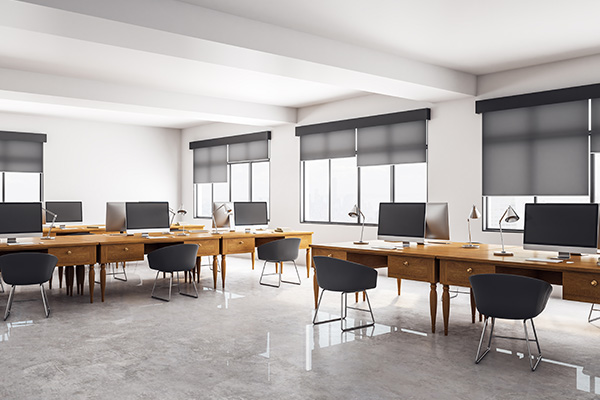 Modern office space with roller blinds on windows and desks arranged for work.