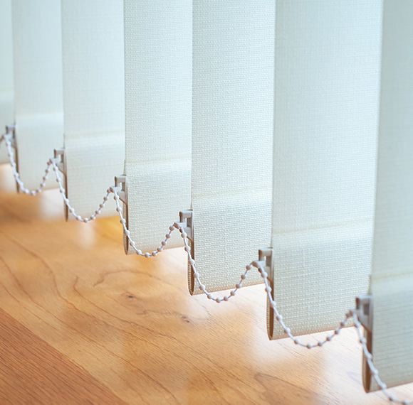 Fabric vertical blinds hung in a bright indoor setting with wooden flooring.