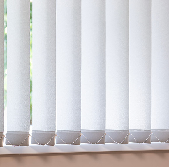 Fabric vertical blinds fitted to a window, allowing light to gently filter through.