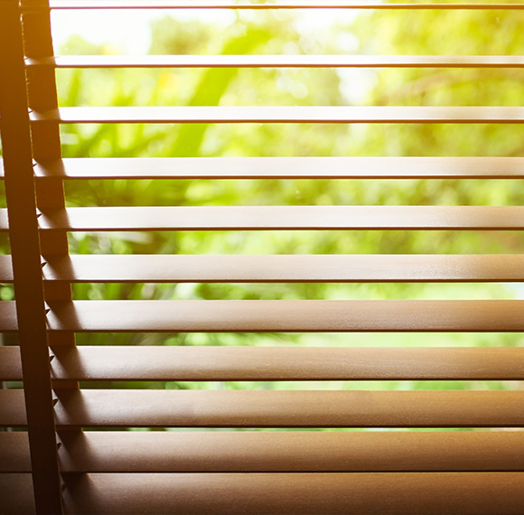 Faux wood blinds partially opened with a blurred green background.