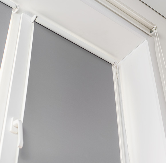 Roller blinds partially covering a window with a gray backdrop in a modern setting.