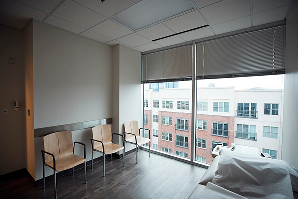 Modern waiting area featuring vertical blinds, wooden chairs, and a view of buildings.
