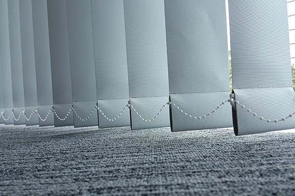 Vertical blinds with a textured design, partially closed over a grey carpet.