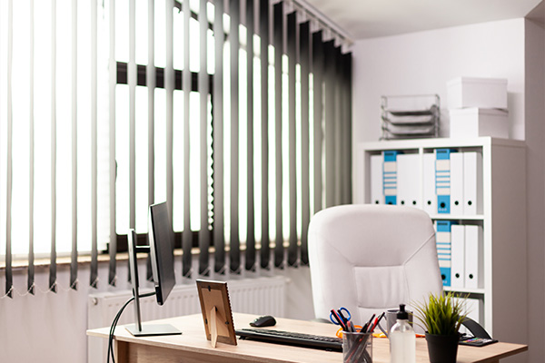 Vertical blinds in a well-lit office with a desk and modern furnishings.