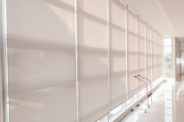 Fabric roller blinds installed in a bright office space with sleek white floors.