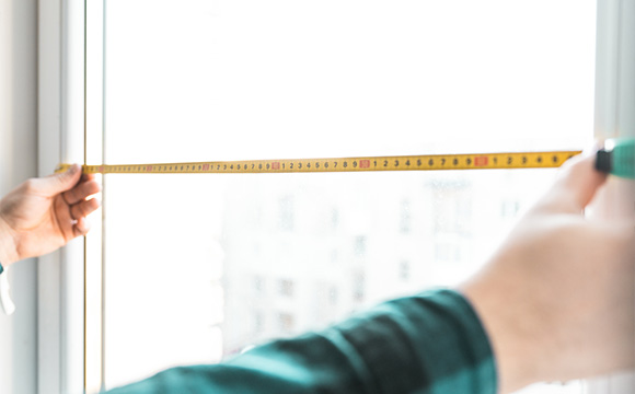Measuring a window with a tape measure for made-to-measure blinds installation.
