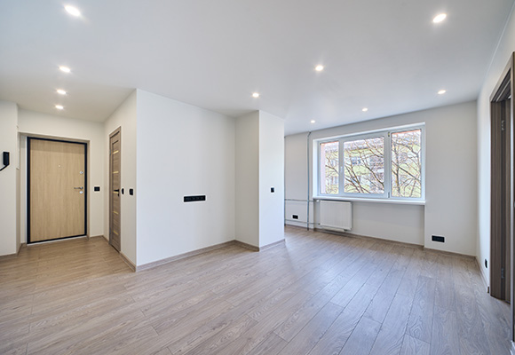 Empty living space with wooden flooring, large window, and modern lighting.