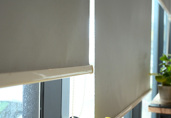 Grey roller blinds installed on window with sunlight filtering through.