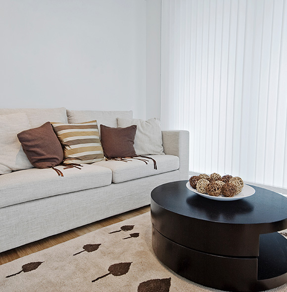 Living room with a beige sofa, patterned cushions, and vertical blinds.