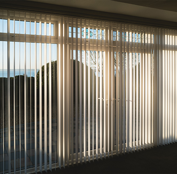 Fabric vertical blinds covering a large window with sunlight coming through.