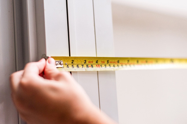 Hand measuring a window frame with yellow tape measure