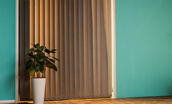 Vertical fabric blinds beside a green wall with a potted plant.