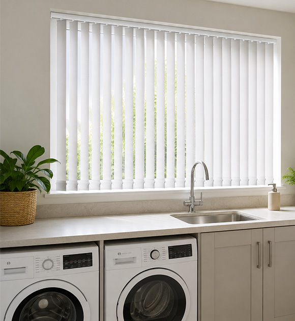White vertical blinds covering a kitchen window above a sink and washing machines.