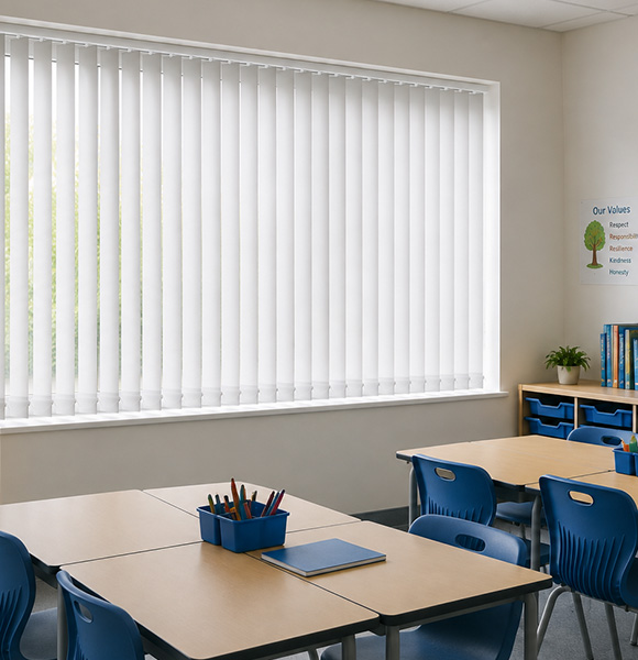 Fabric vertical blinds covering a large classroom window with blue furniture and stationery.