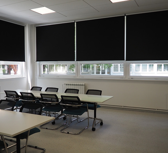 Blackout roller blinds installed in a modern office space with tables and chairs.