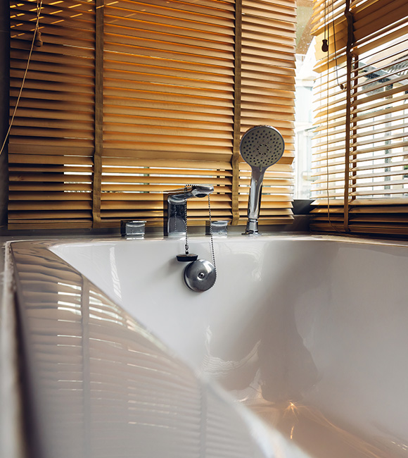 Fauxwood blinds above a modern bathtub with a chrome faucet and showerhead.