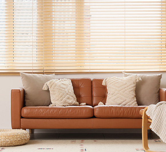 Light wood blinds above a leather sofa with decorative pillows in a modern room.