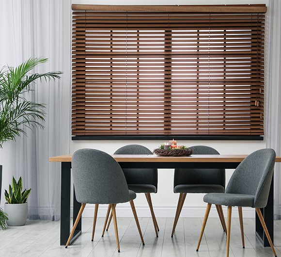 Wooden Venetian blinds installed in a modern dining area with a table and chairs.