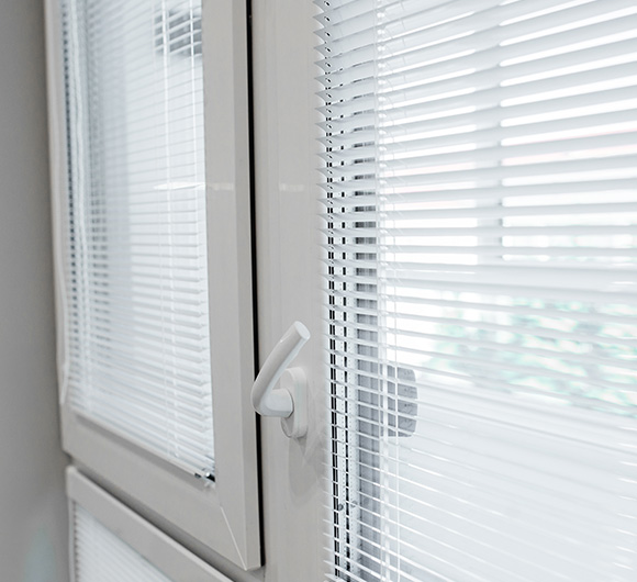 White horizontal blinds partially closed on a window with a handle, showcasing a modern interior.